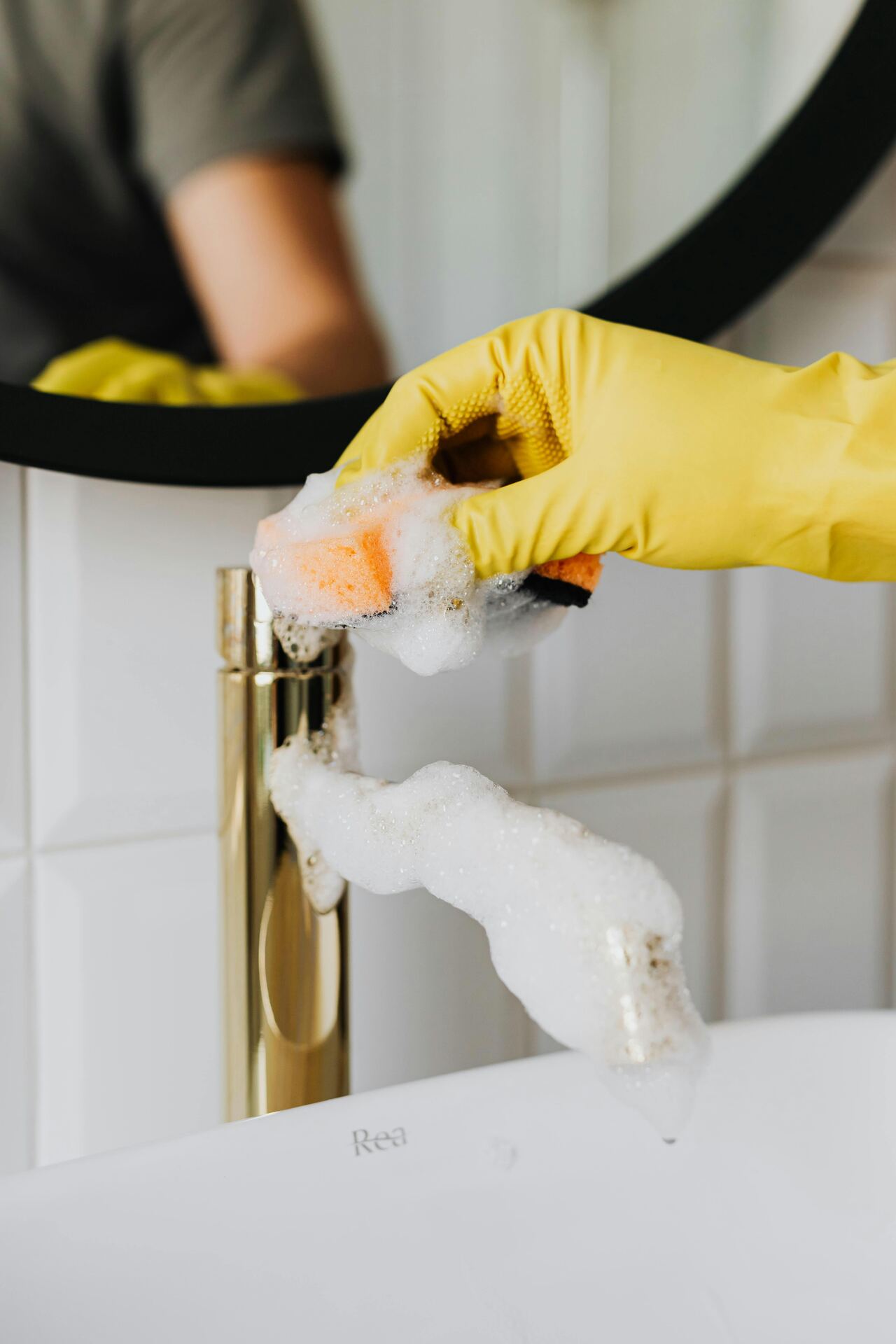Gloved hand cleaning a bathroom faucet